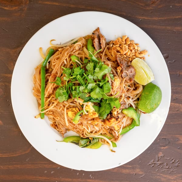 Vietnam Express's Pad See Ew with noodles, beef, vegetables, peanuts, and lime on a white plate.