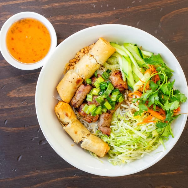 Overhead view of a Vietnamese vermicelli bowl with grilled pork, spring rolls, and fresh vegetables.