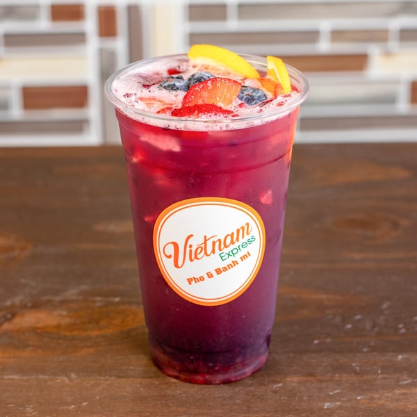 A vibrant berry iced tea from Vietnam Express, garnished with fresh strawberries, blueberries, and orange slices.