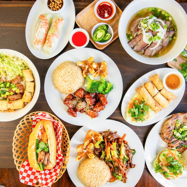 A top-down view of various Vietnamese dishes, including pho, spring rolls, rice, and a banh mi.